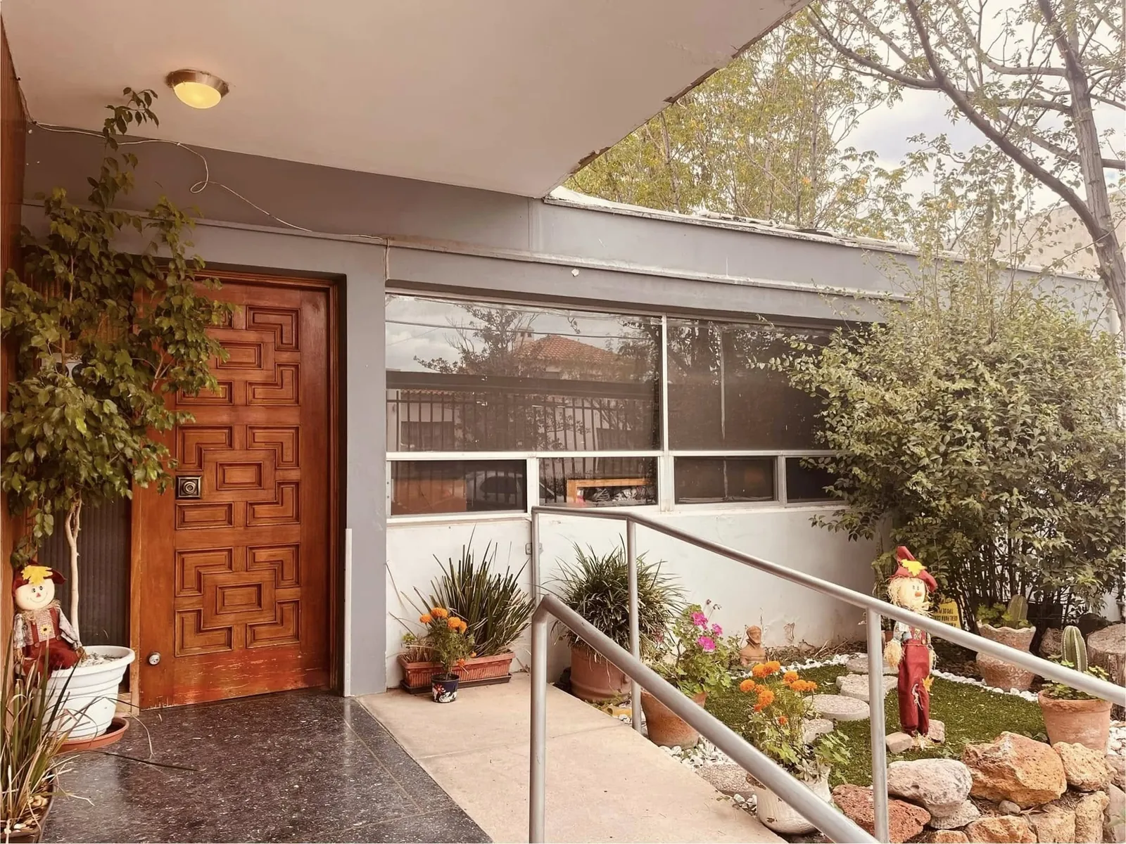 Fachada de entrada de Asilo Los Geranios, residencia para adultos mayores en Chihuahua, con puerta de madera, rampa y jardín