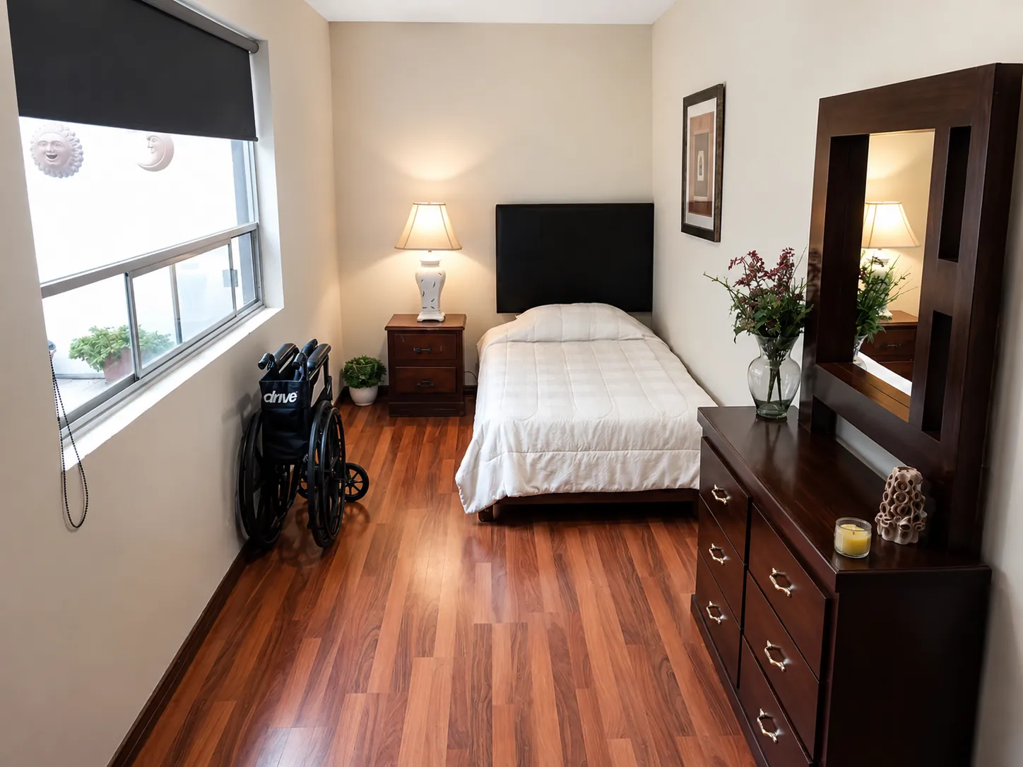 Habitación con cama, cómoda, espejo y silla de ruedas adaptada en asilo en Chihuahua