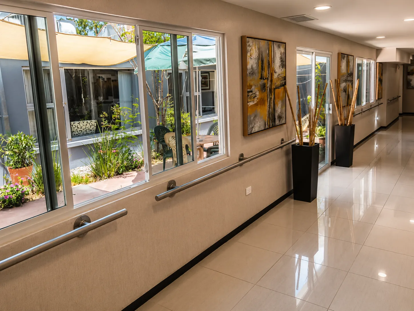 Pasillo con pasamanos y ventanales al patio en residencia para adultos mayores en Chihuahua